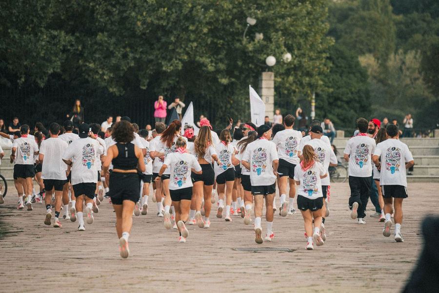 A large group of runners in white tees setting off together in Milan