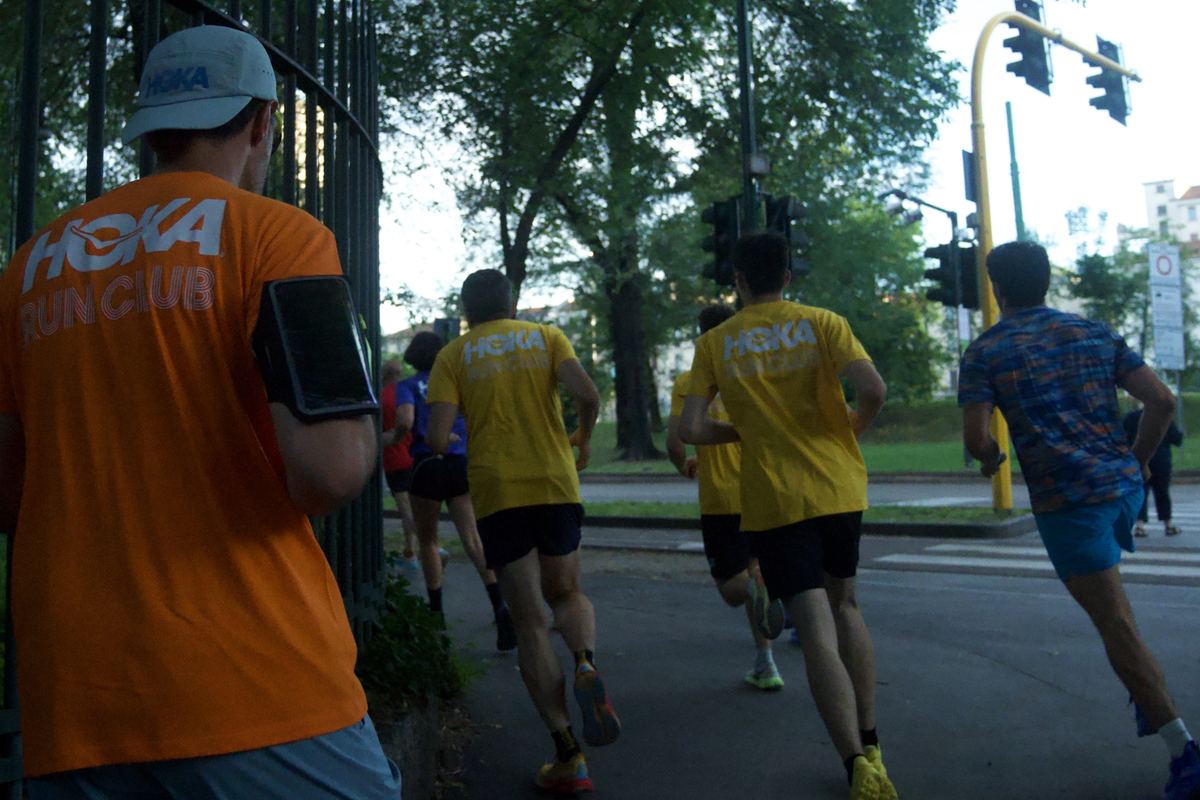 Runners in HOKA Run Club tees heading out along a park fence
