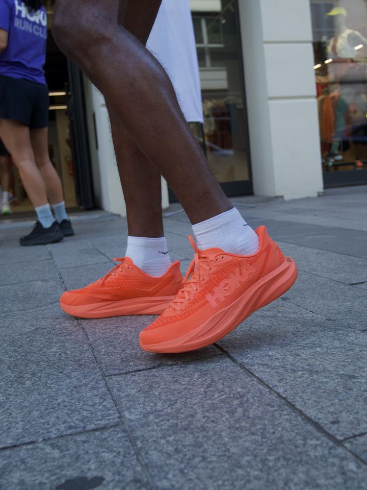 Close-up of an all-orange HOKA running shoe on a runner outside the store