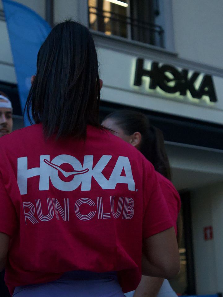 The back of a red HOKA Run Club tee with the HOKA store sign behind