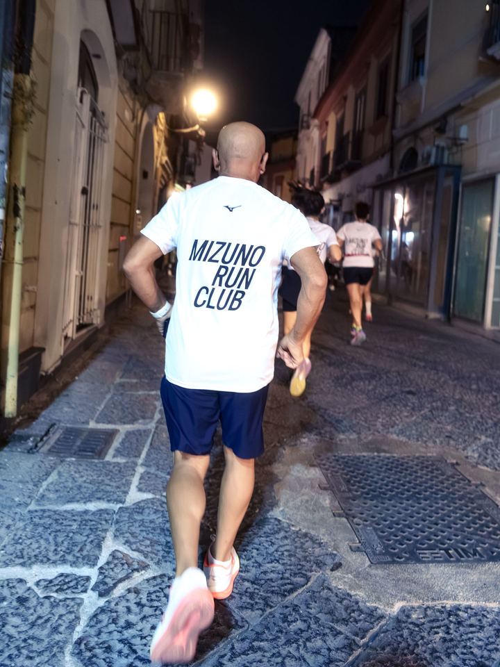 A runner in a Mizuno Run Club tee seen from behind on a cobbled street