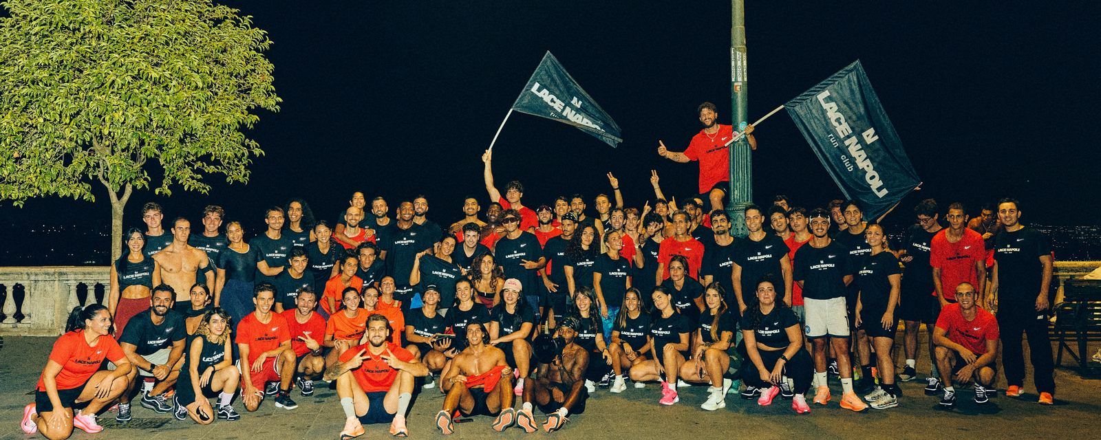 The LACE Napoli crew at night in black and red LACE Napoli tees with the Nike swoosh, waving two LACE Napoli run club flags