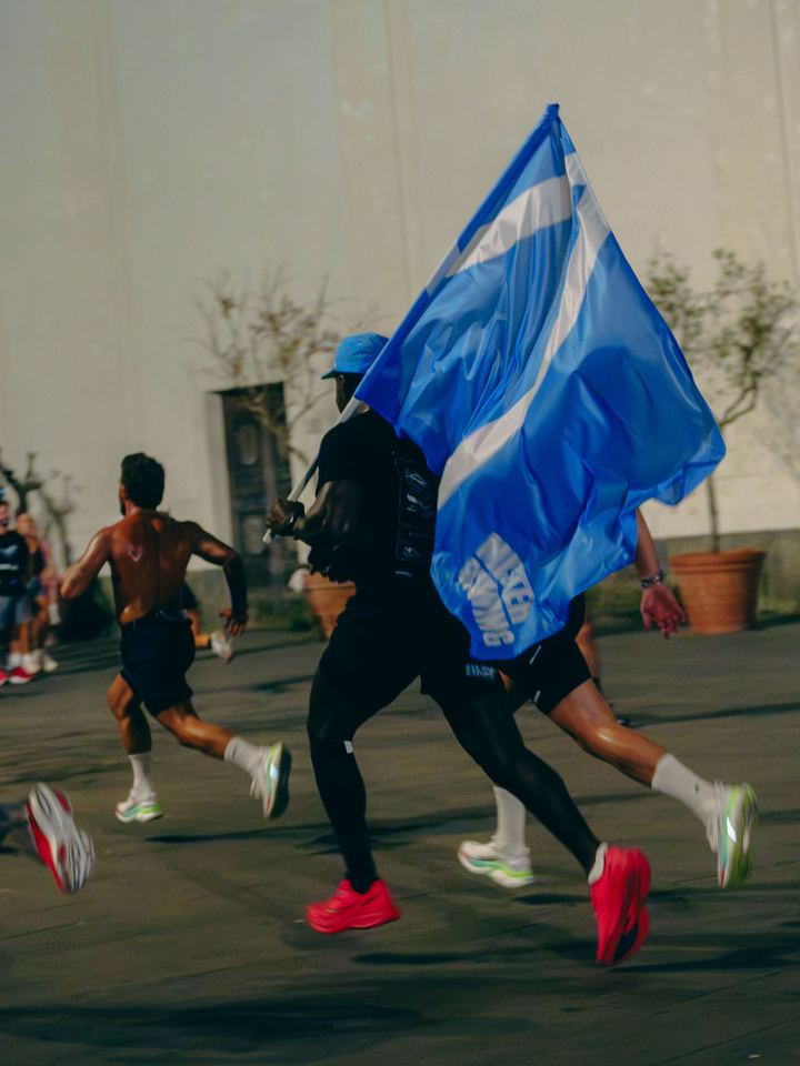 A runner carrying a blue Mister Running flag mid-stride